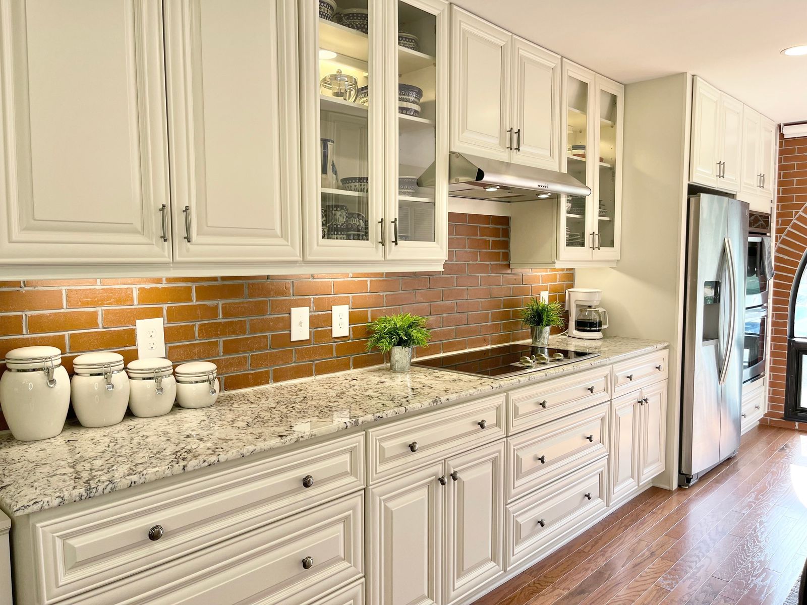 Kitchen with D9 Pearl White raised-panel cabinets, glass uppers and exposed brick backsplash
