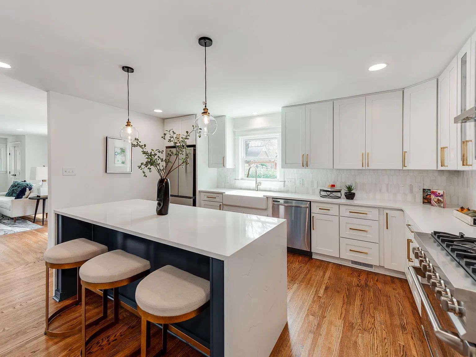White shaker kitchen with a navy island, upholstered stools and black pendants